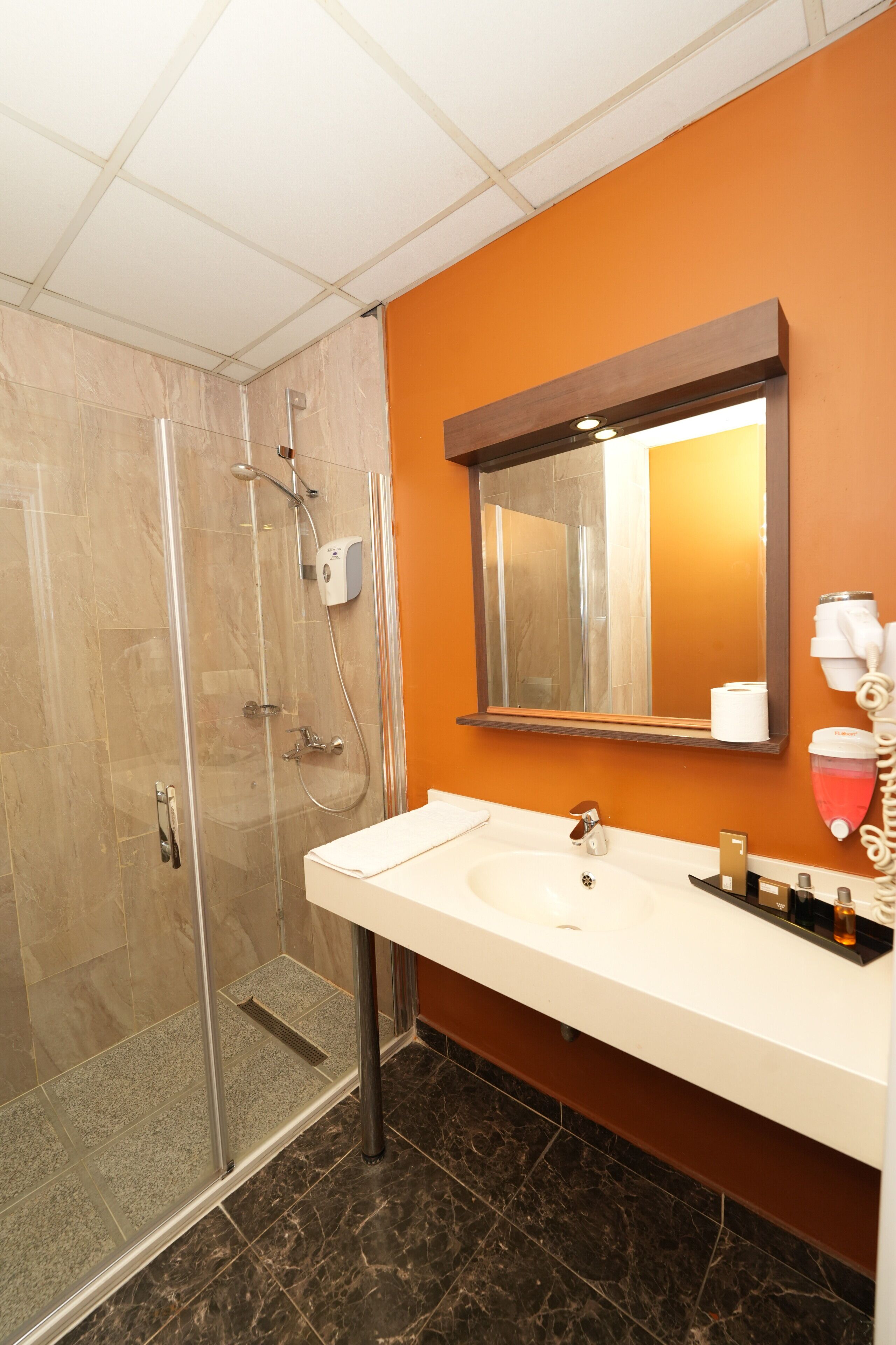 A bathroom with a glass shower enclosure, a white sink, and an orange wall.