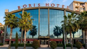 Un hotel con fachada de vidrio amplia, palmeras y un cartel llamativo que dice 'BORIS HOTEL'.