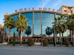Un hotel con fachada de vidrio amplia, palmeras y un cartel llamativo que dice 'BORIS HOTEL'.