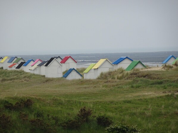Une rangée de cabanes de plage aux toits colorés, disposées en ligne le long de la côte.