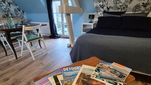A bedroom with a bed, a wooden coffee table with magazines, a desk with a chair, and a window with a view of the outside. - Normandy Couple Getaway With Garden (Saint-Sauveur-Villages)