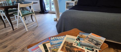 Ein Schlafzimmer mit einem Bett, einem Holztisch mit Zeitschriften, einem Schreibtisch mit Stuhl und einem Fenster mit Außenblick.