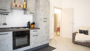 Eine moderne Küche mit Gasherd, Backofen und grauen Schränken. Auf der Arbeitsfläche befinden sich eine Kaffeemaschine und ein Messerblock.