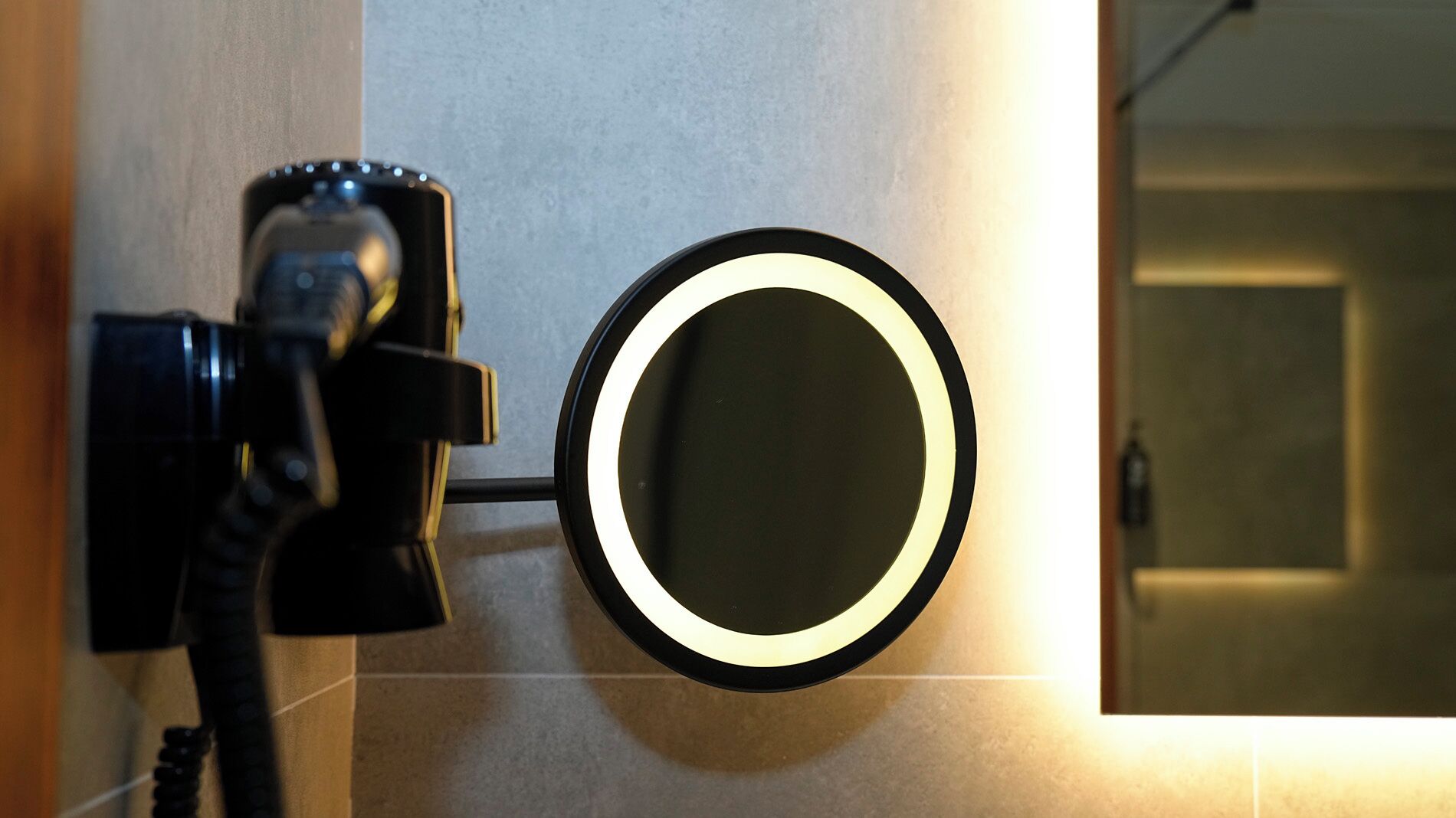 Um banheiro com secador de cabelo fixado na parede e um espelho redondo com iluminação.