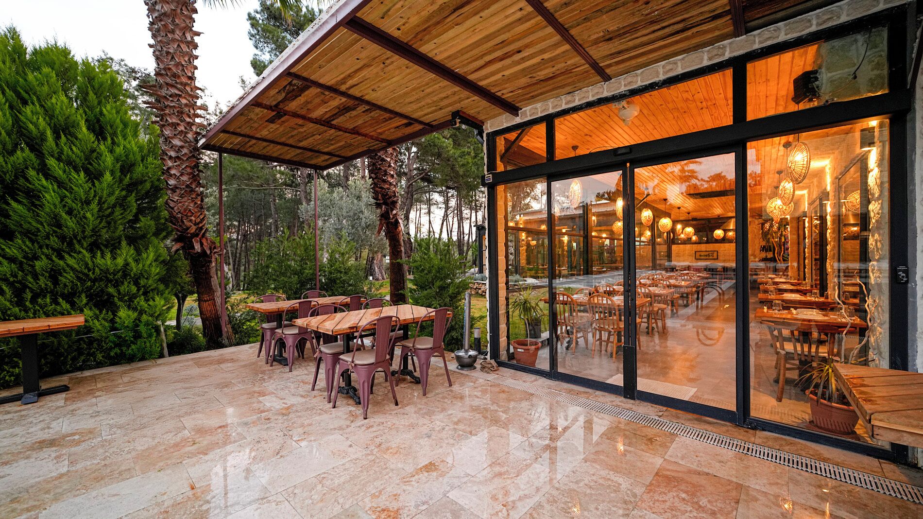 Un espace de restauration en plein air, avec des tables et des chaises en bois, entouré de verdure et doté d’un sol carrelé en pierre.
