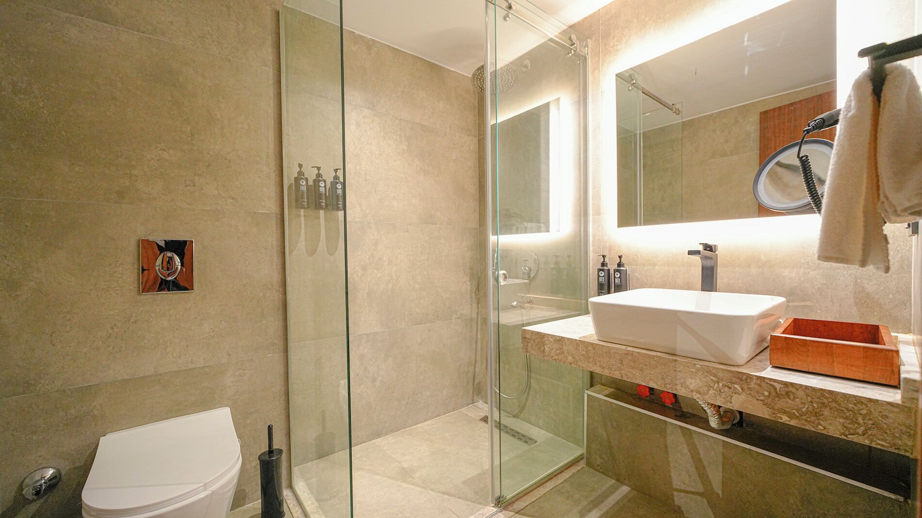 Un baño moderno con ducha de vidrio, inodoro blanco y tocador con lavamanos grande y espejo.