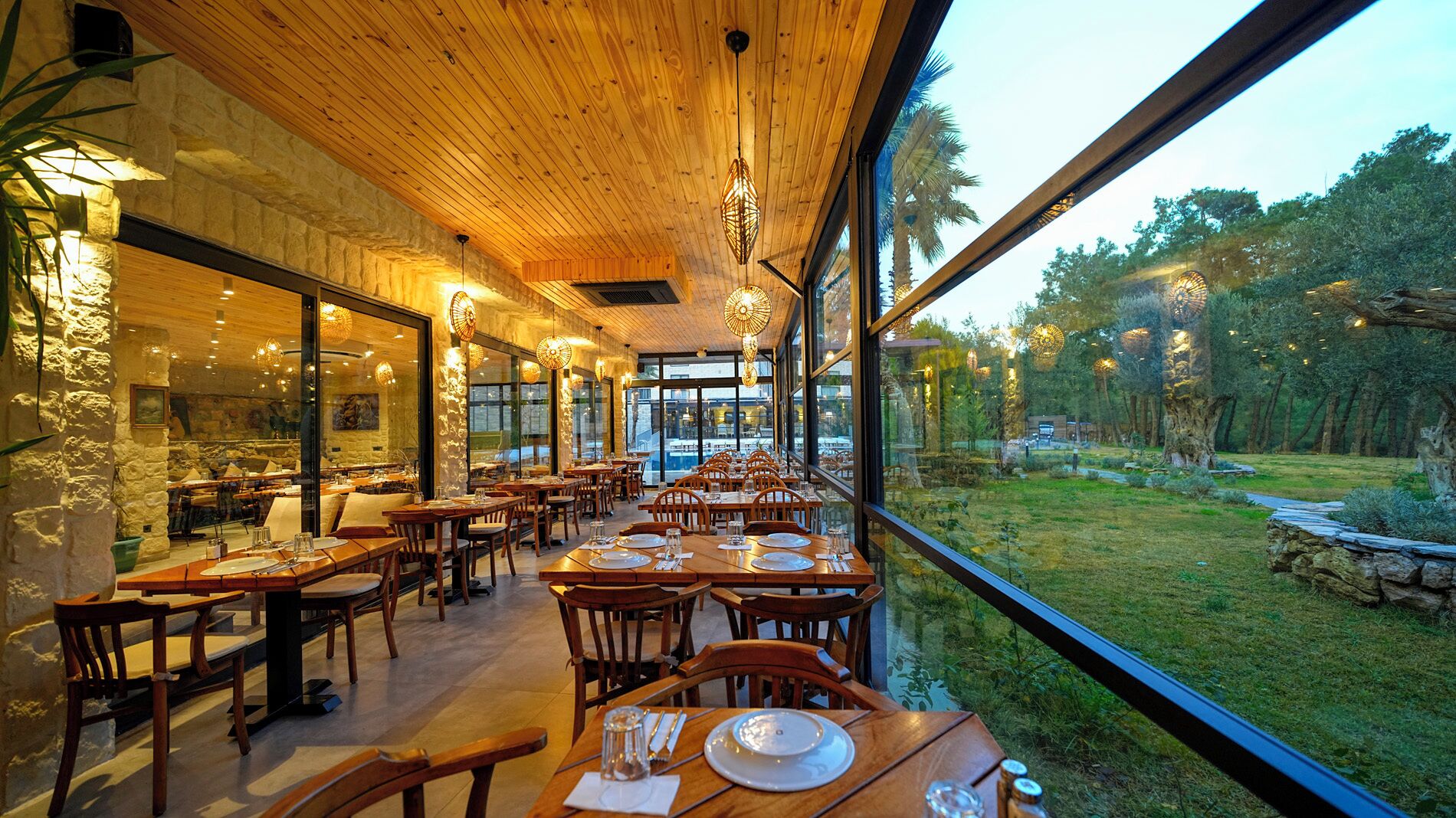 A restaurant with wooden interiors, large windows, and a view of a grassy area.