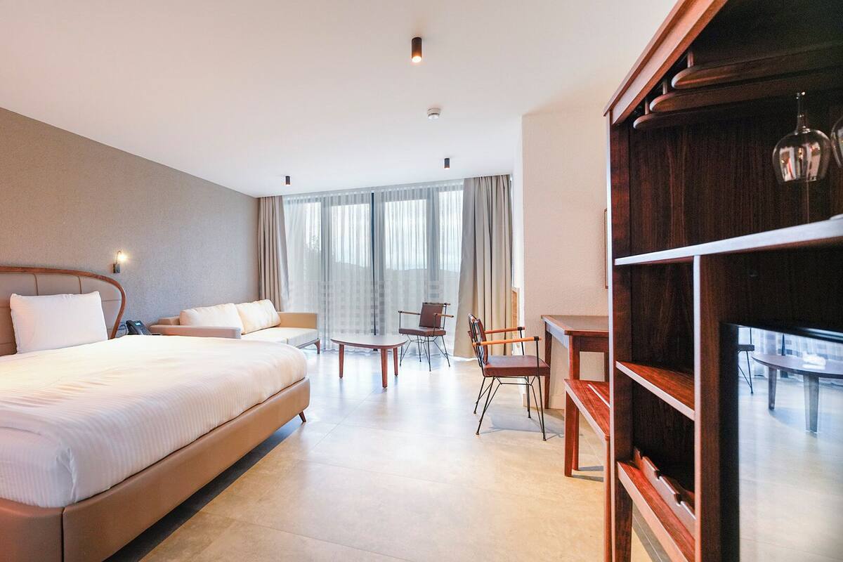 A hotel room with a large bed, a desk, a chair, and a bookshelf.