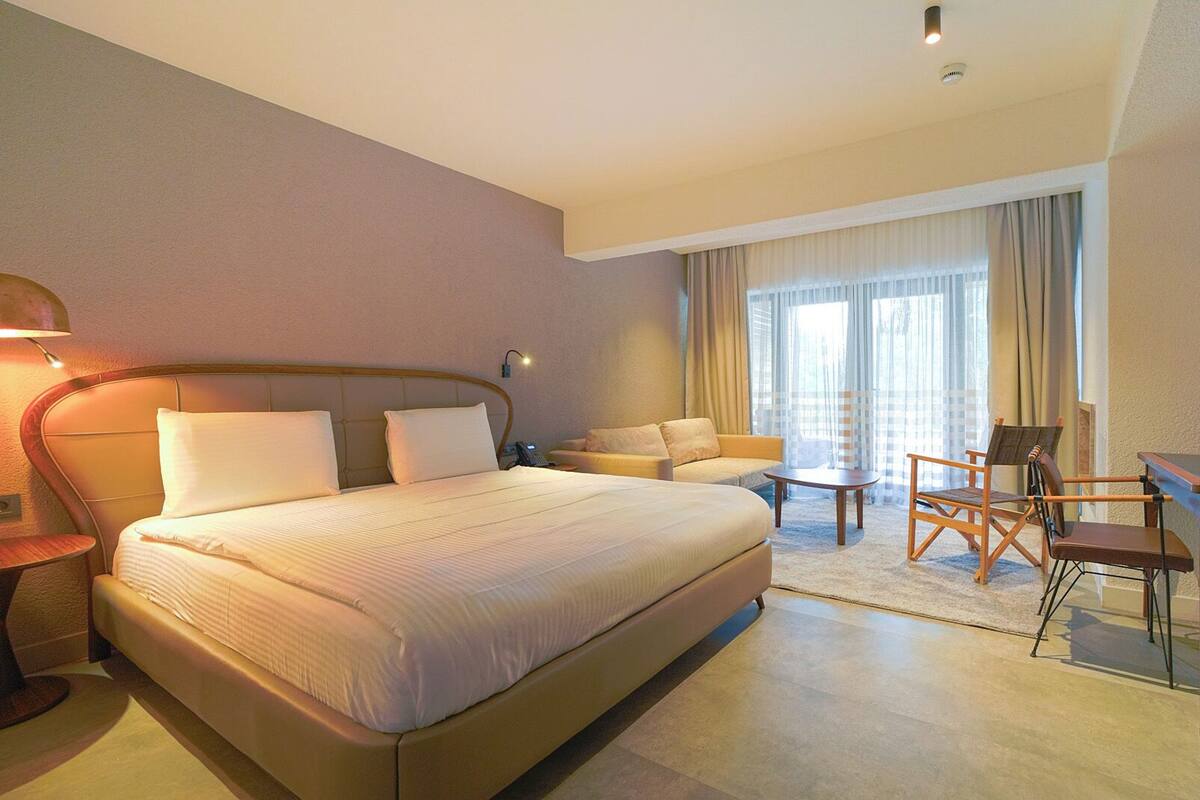 A hotel room with a large bed, a desk, a chair, and a sofa.