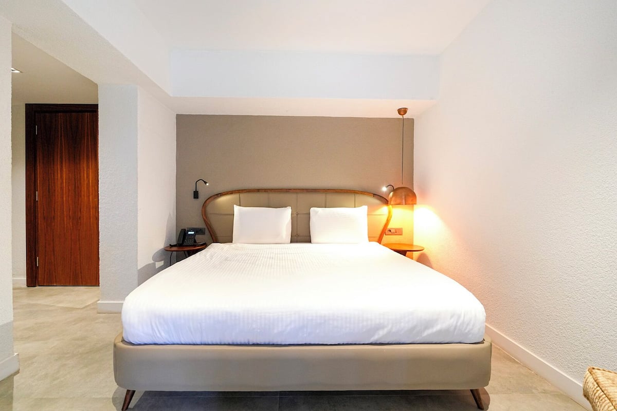 A hotel room with a large bed, a bedside table with a lamp, and a wooden door.