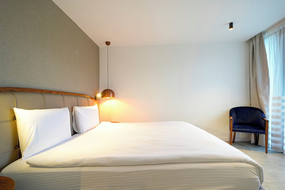 A hotel room with a large bed, a chair, and a window with curtains.