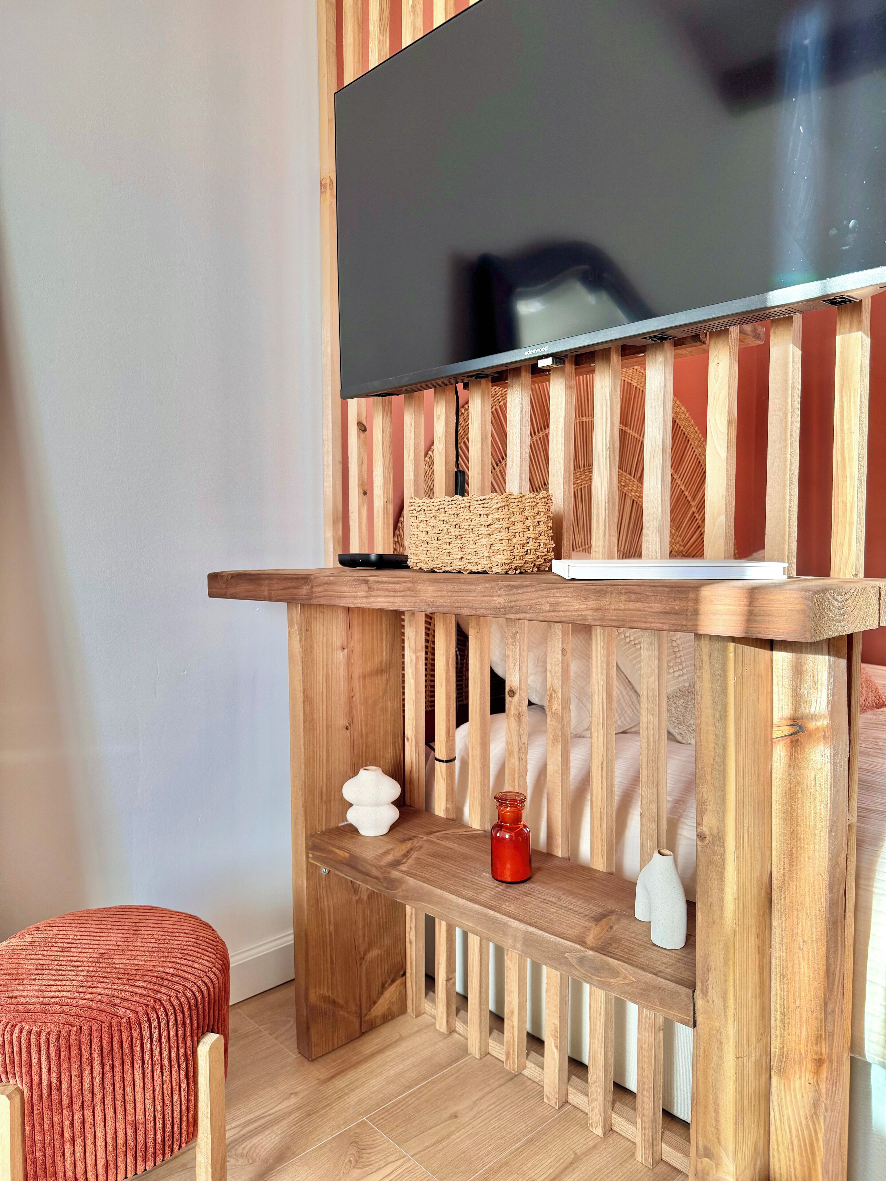 Un meuble en bois pour la télévision, sur lequel est posée une télévision à écran plat, ainsi qu’un panier en osier et une petite table agrémentée d’objets décoratifs.