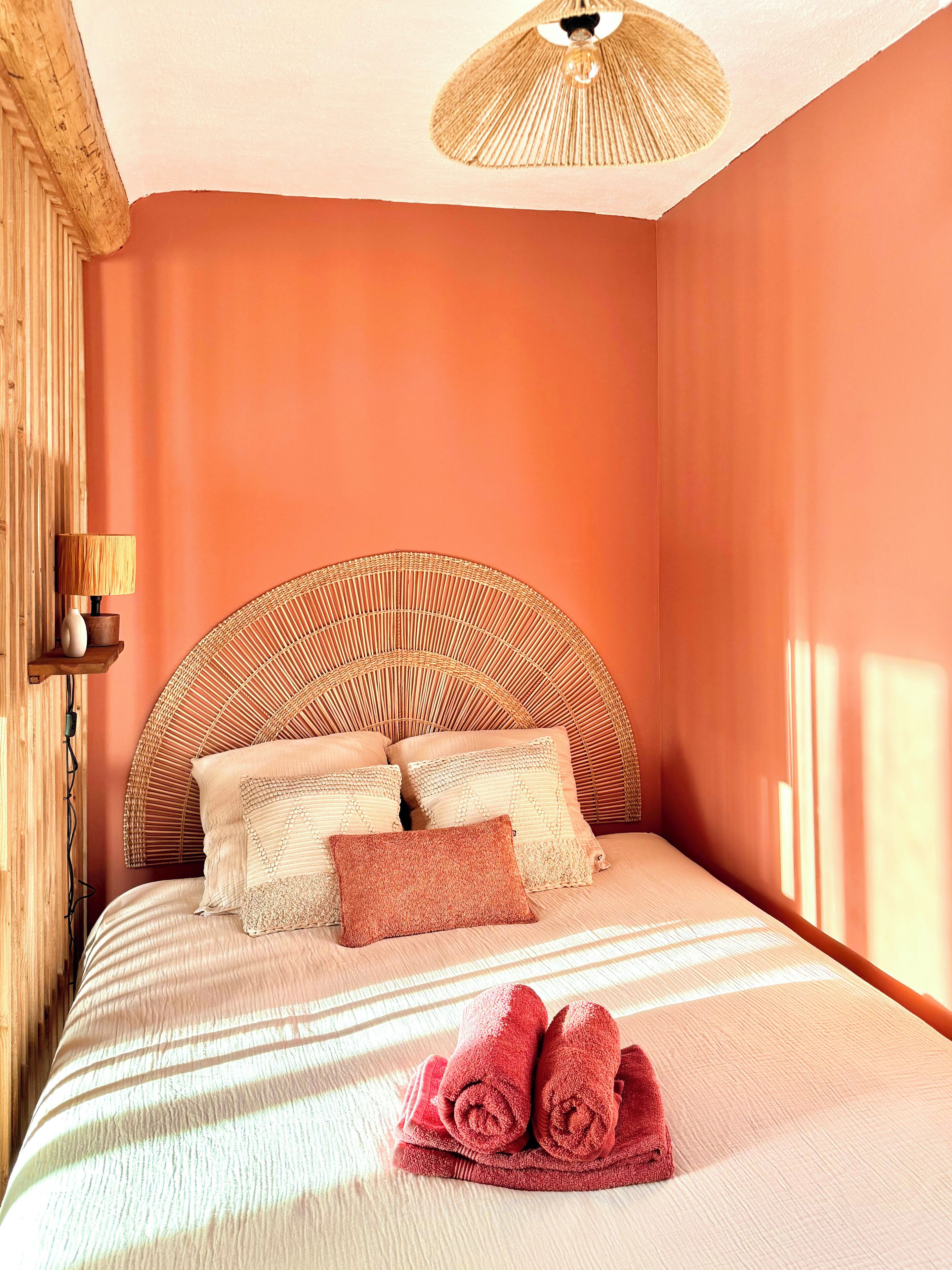 A bedroom with a bed, pillows, a lamp, and a wall-mounted shelf.