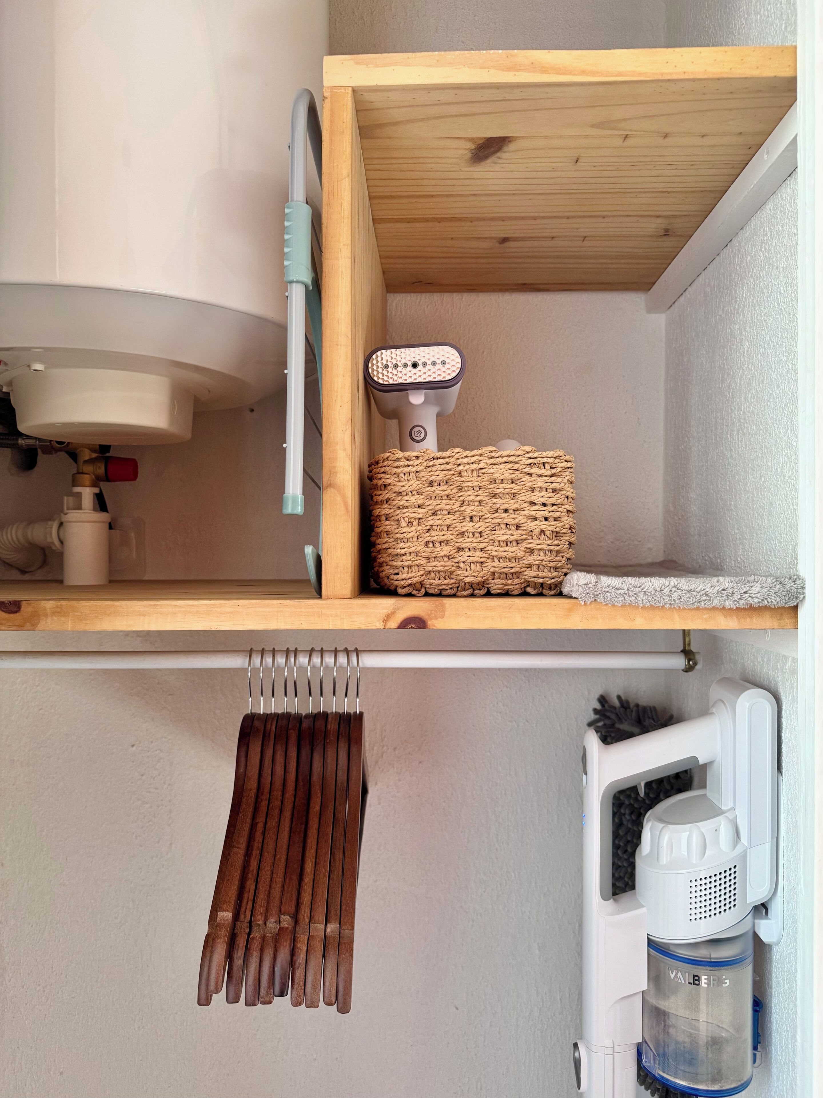 A bathroom with a wooden shelf holding a woven basket and a towel, a toilet, a hand dryer, and a water dispenser.