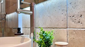 Een badkamer met een wit wastafelmeubel, een moderne kraan, een plant in pot en een glazen pot met een borstel.
