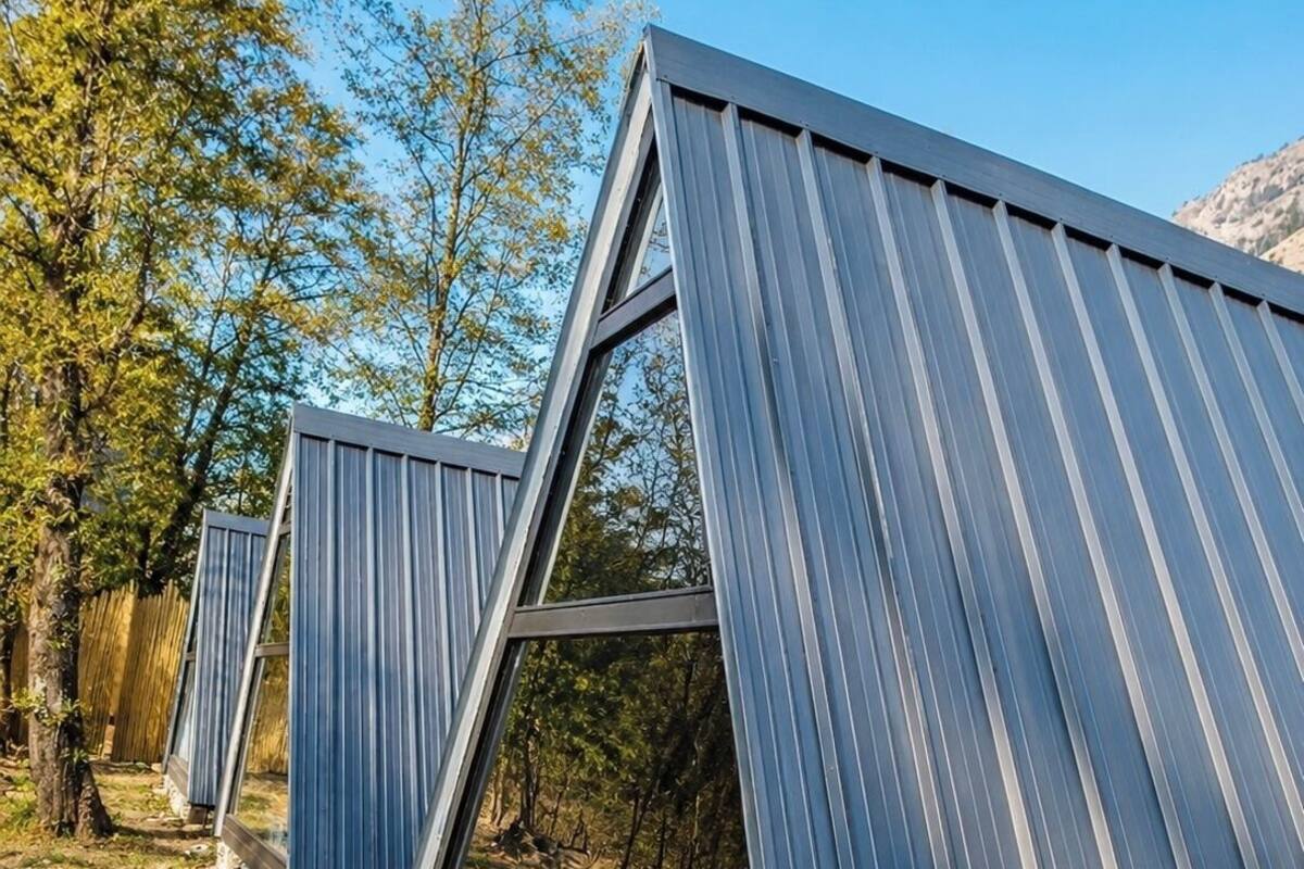 A series of modern, triangular metal structures with large windows, set in a natural, wooded area.