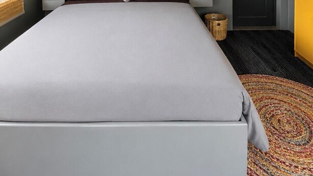 Une chambre à coucher comprenant un lit, des tables de chevet, un ventilateur de plafond, une porte et une fenêtre avec des stores.