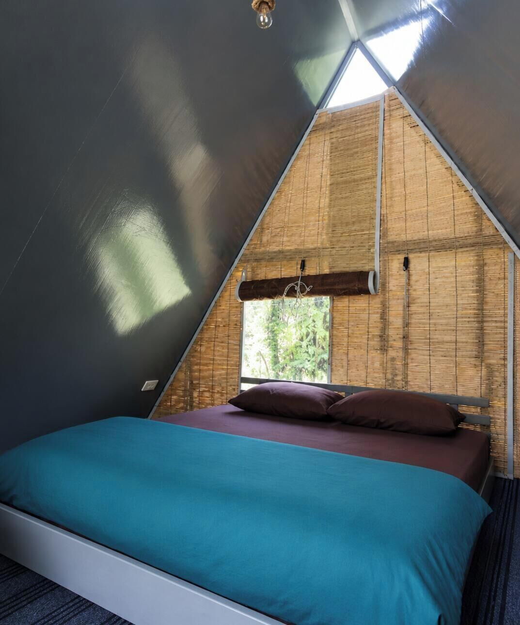 A triangular tent with a bed, a window, and a hanging light fixture.