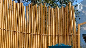 Une clôture en bambou avec une structure bleue qui semble être un espace réservé aux toilettes ou aux équipements techniques.
