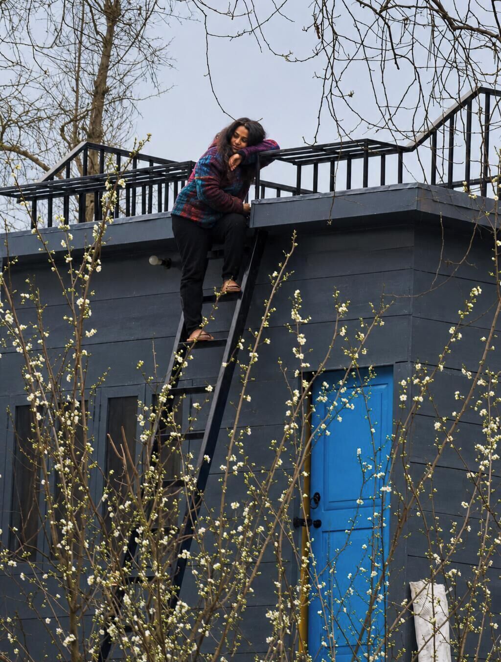 A person climbing a metal ladder on a building with a blue door.