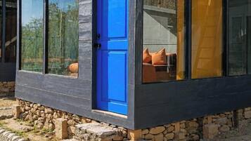 Un edificio moderno de una sola planta con puerta azul y ventanas amplias, rodeado de una base de piedra y un camino de grava.