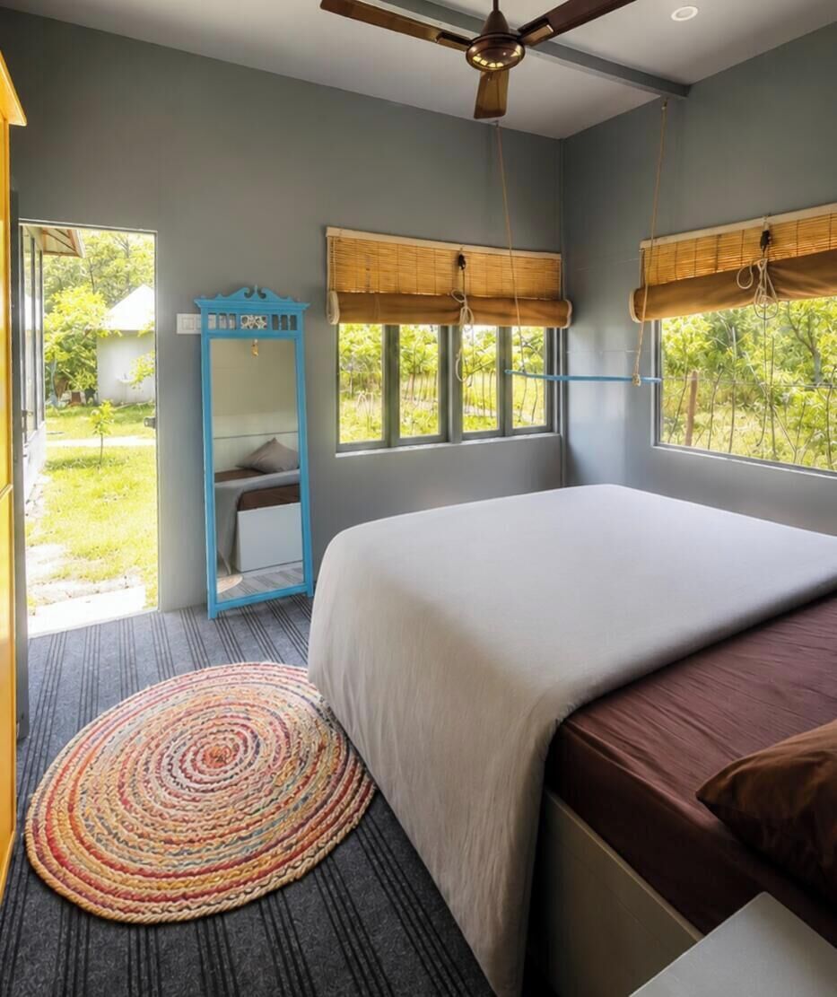 A bedroom with a bed, a ceiling fan, a window with a view of greenery, and a mirror.