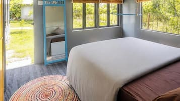 A bedroom with a bed, a ceiling fan, a window with a view of greenery, and a mirror.