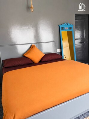 A bed with an orange bedspread and two pillows, a wall-mounted light fixture, and a blue mirror leaning against the wall. - The Soul Stop by evaddo stays (Aut)