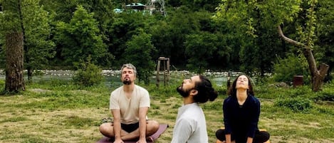 Three individuals practicing yoga on mats outdoors with a mountainous backdrop.