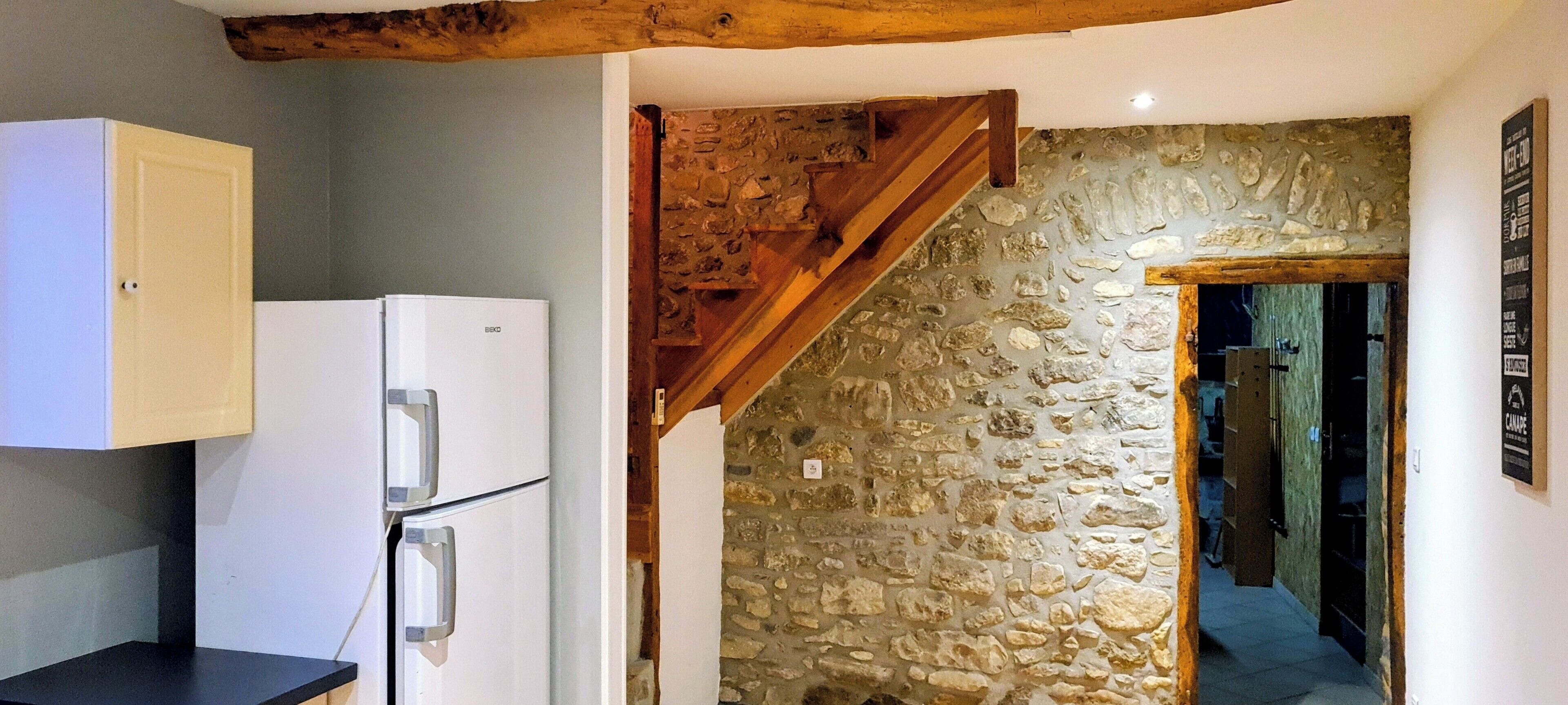 A kitchen with a white refrigerator, a wooden ceiling, and a stone wall.