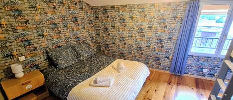 Une chambre avec un mur décoré d’un motif en briques, un lit recouvert d’une couverture blanche, une table de chevet avec une lampe et une fenêtre avec des rideaux.