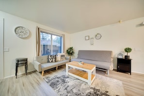 A modern living room with a sofa, a coffee table, a side table, a clock, and a window with curtains.