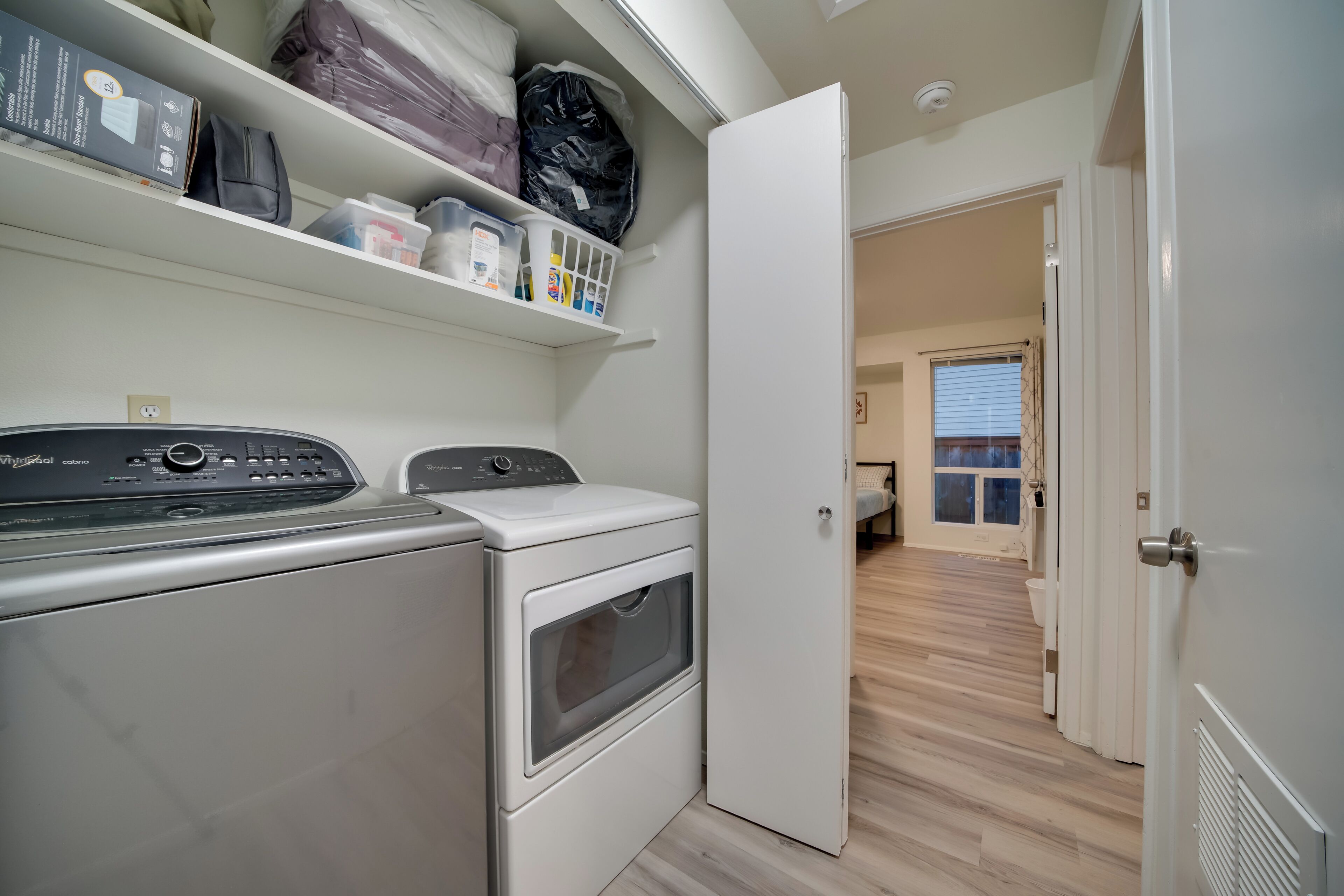 A laundry area with a washing machine and dryer, shelves with storage bins, and a door leading to another room.