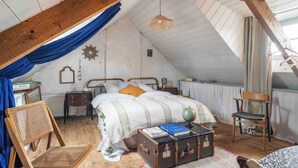 Un dormitorio acogedor en el ático, con techo inclinado, una cama de madera, una silla, una maleta y un globo terráqueo.
