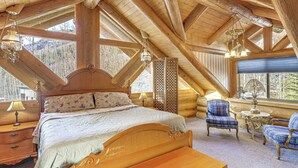 Une chambre située dans un chalet en rondins, avec un grand lit, deux fauteuils, une petite table et un lustre.