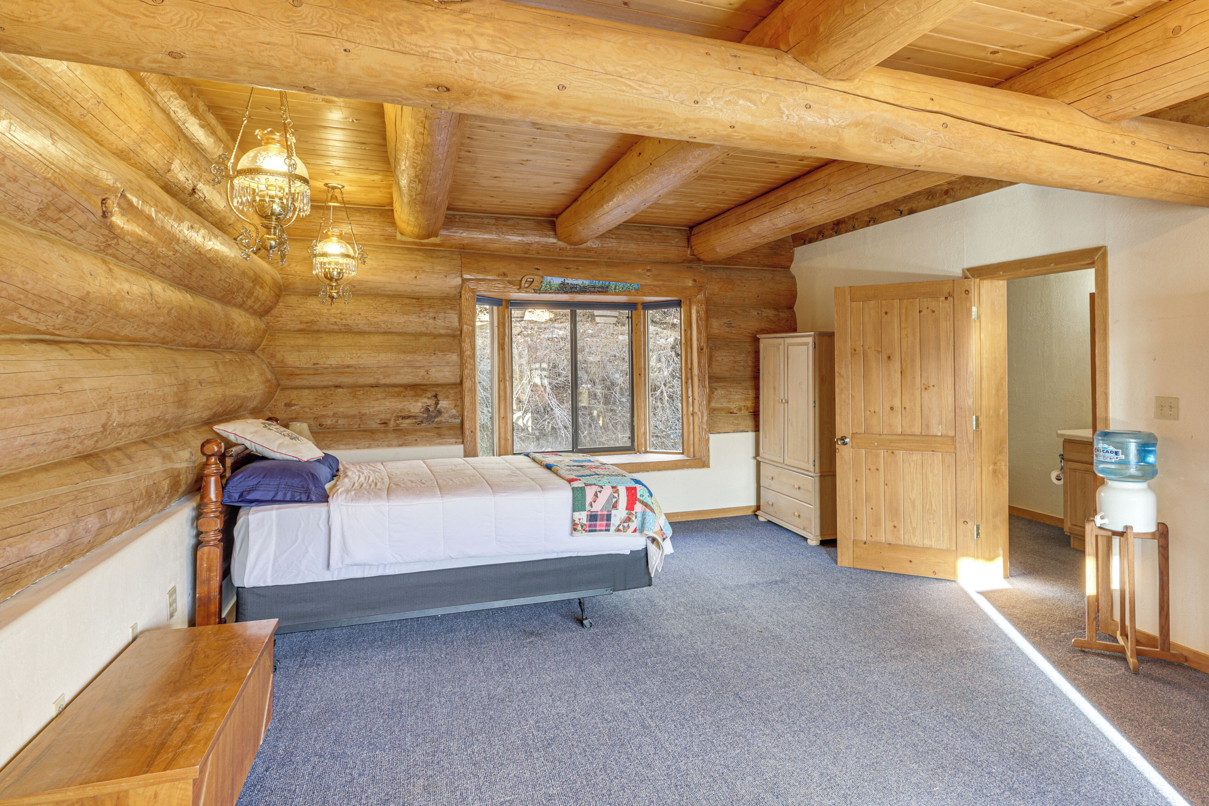 A log cabin bedroom with a bed, wooden walls, a window, and a wooden door.