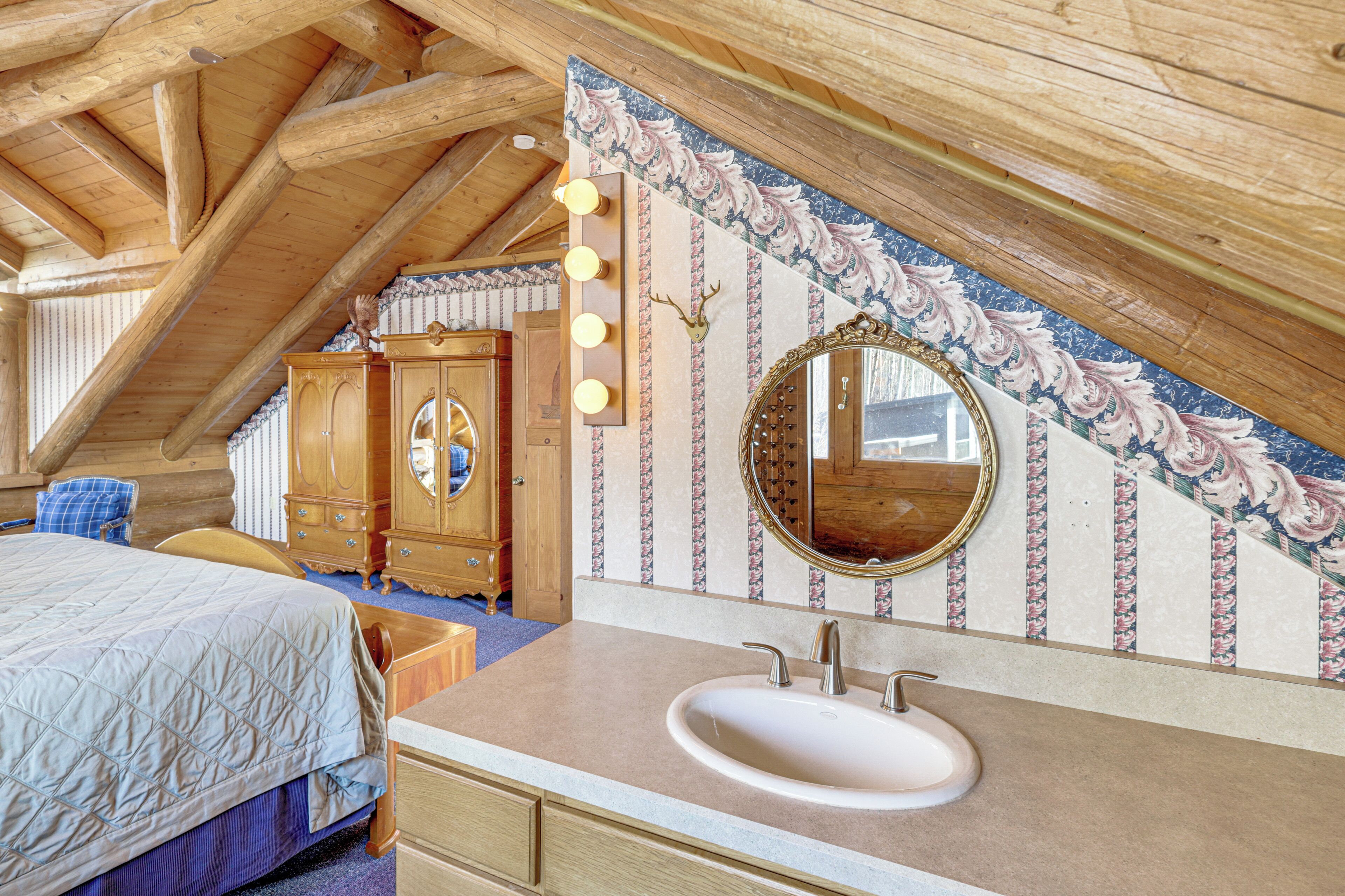 A bedroom with a wooden ceiling, a large bed, a vanity with a mirror, and a dresser.