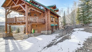 Une cabane en rondins dotée d’un balcon, avec des fondations en pierre et un sol recouvert de neige.