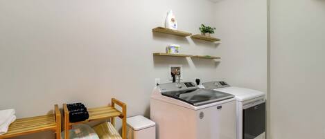 Un área de lavandería con lavadora, secadora y un estante con productos de limpieza.