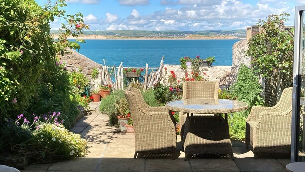A patio with wicker furniture and potted plants, overlooking a coastal view. - Mariners Cottage (Bideford)