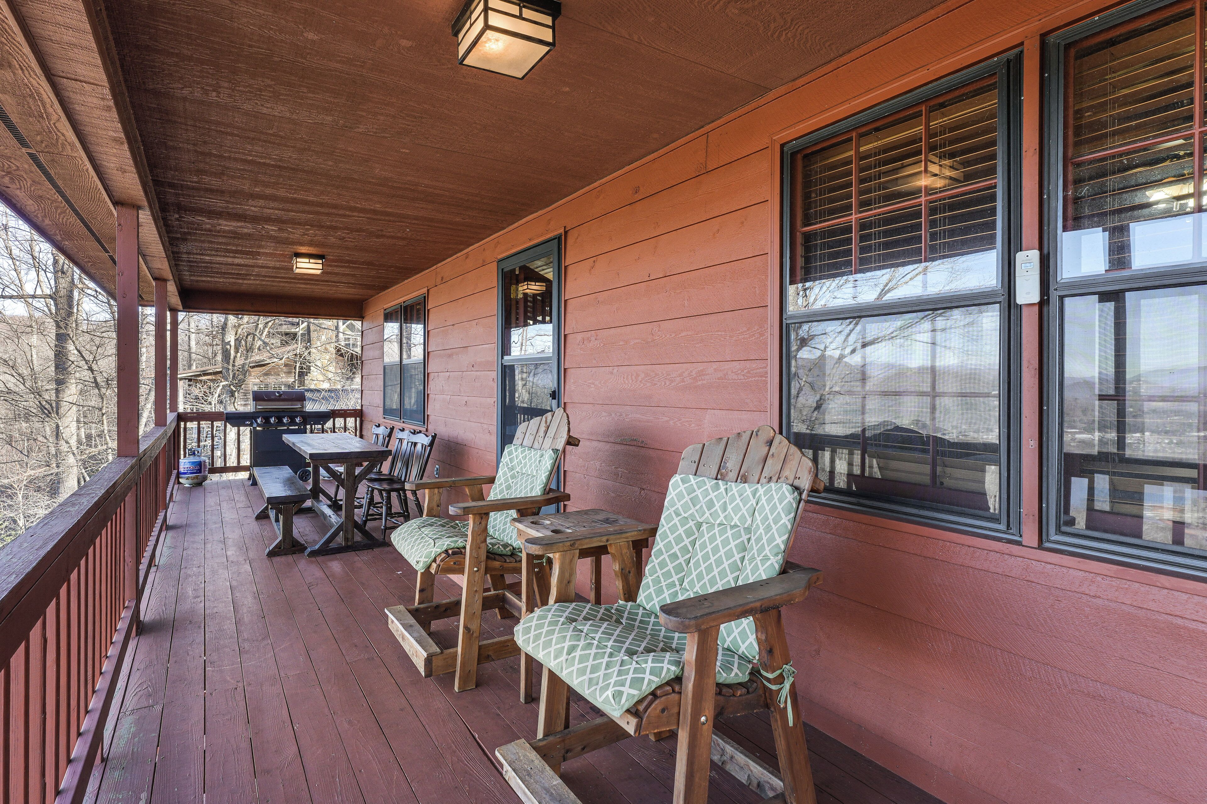 A wooden porch with a table and chairs, a grill, and large windows.
