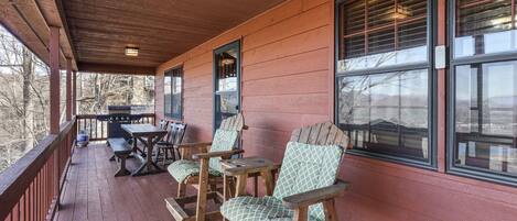 A wooden porch with a table and chairs, a grill, and large windows.