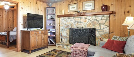 A cozy living room with a stone fireplace, wooden walls, a television, and a comfortable sofa.