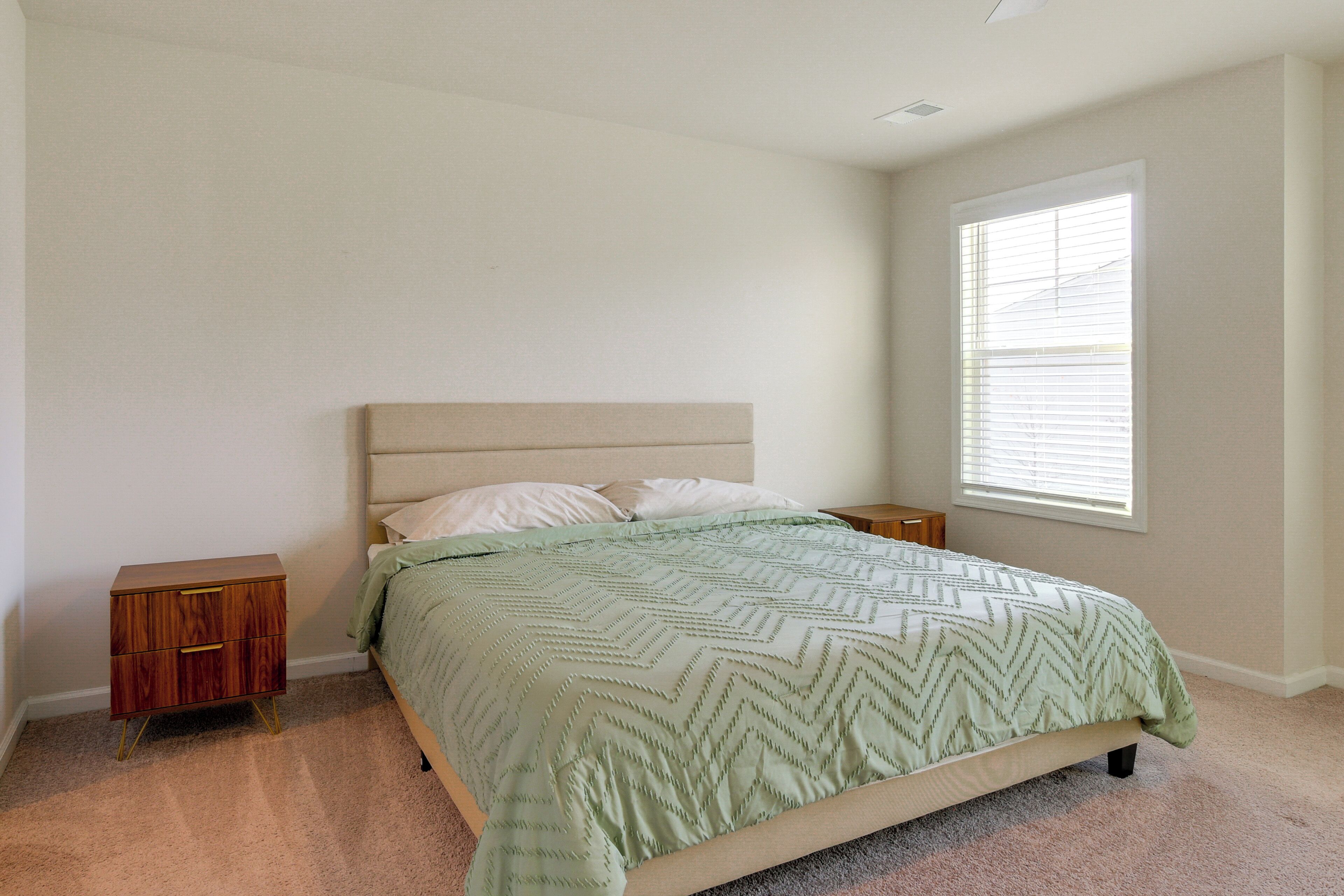 A bedroom with a bed, nightstands, a window, and a carpeted floor.