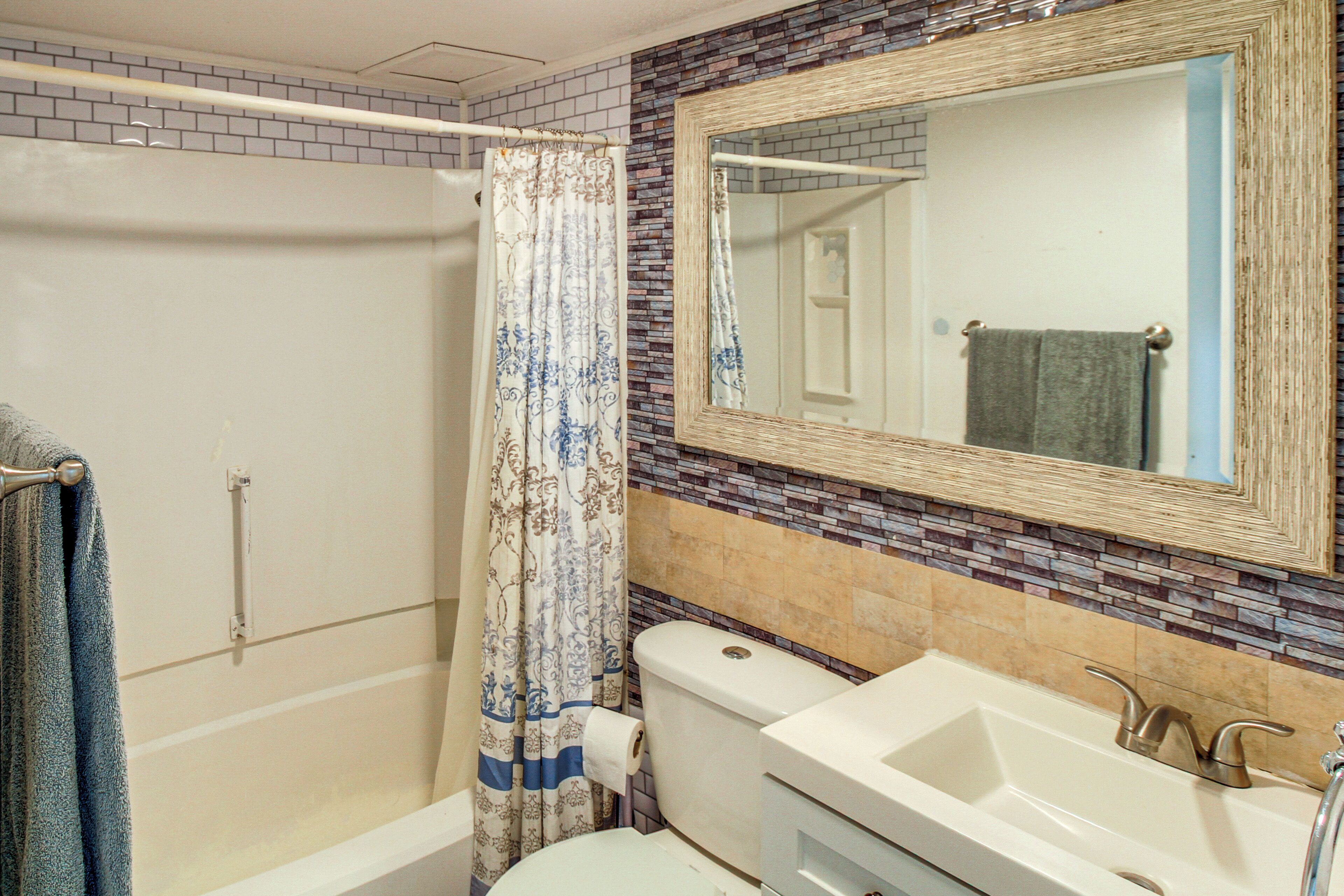 Een badkamer met douche, toilet, wastafel en spiegel.