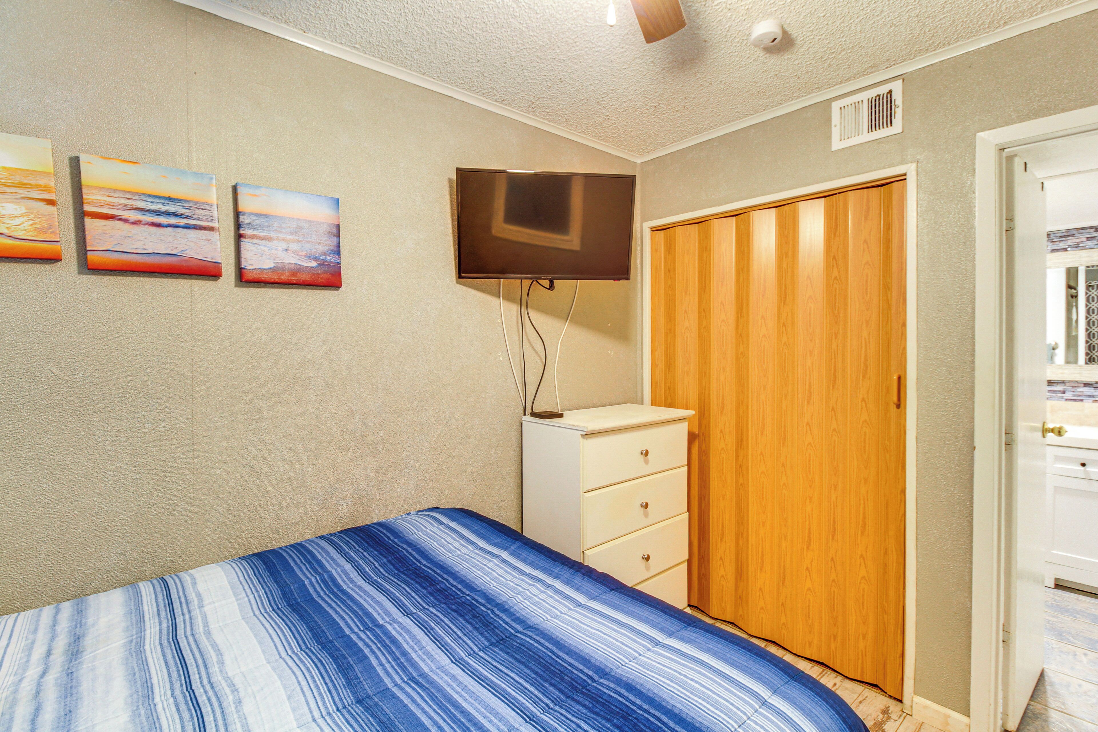 Un dormitorio con una cama, un televisor montado en la pared, un armario de madera y un aparador blanco.