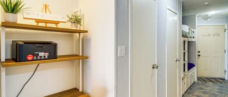 Un pasillo con un banco de madera, una impresora y estanterías con plantas y un cartel.