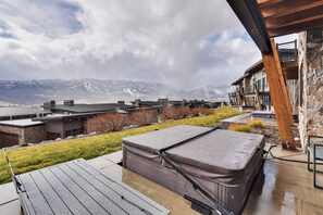 Een wellnessruimte met een jacuzzi, houten terras en uitzicht op bergen.