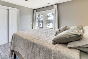 A bedroom with a large bed, a window with curtains, and a view of trees and water outside.