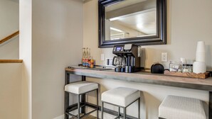 Una zona de bar con una máquina de café, dos taburetes y un espejo sobre la barra.